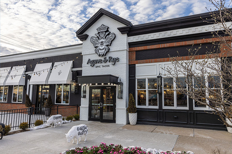 The exterior of Agave & Rye restaurant with a white and black facade, large windows, and decorative statues of white pigs near the entrance.