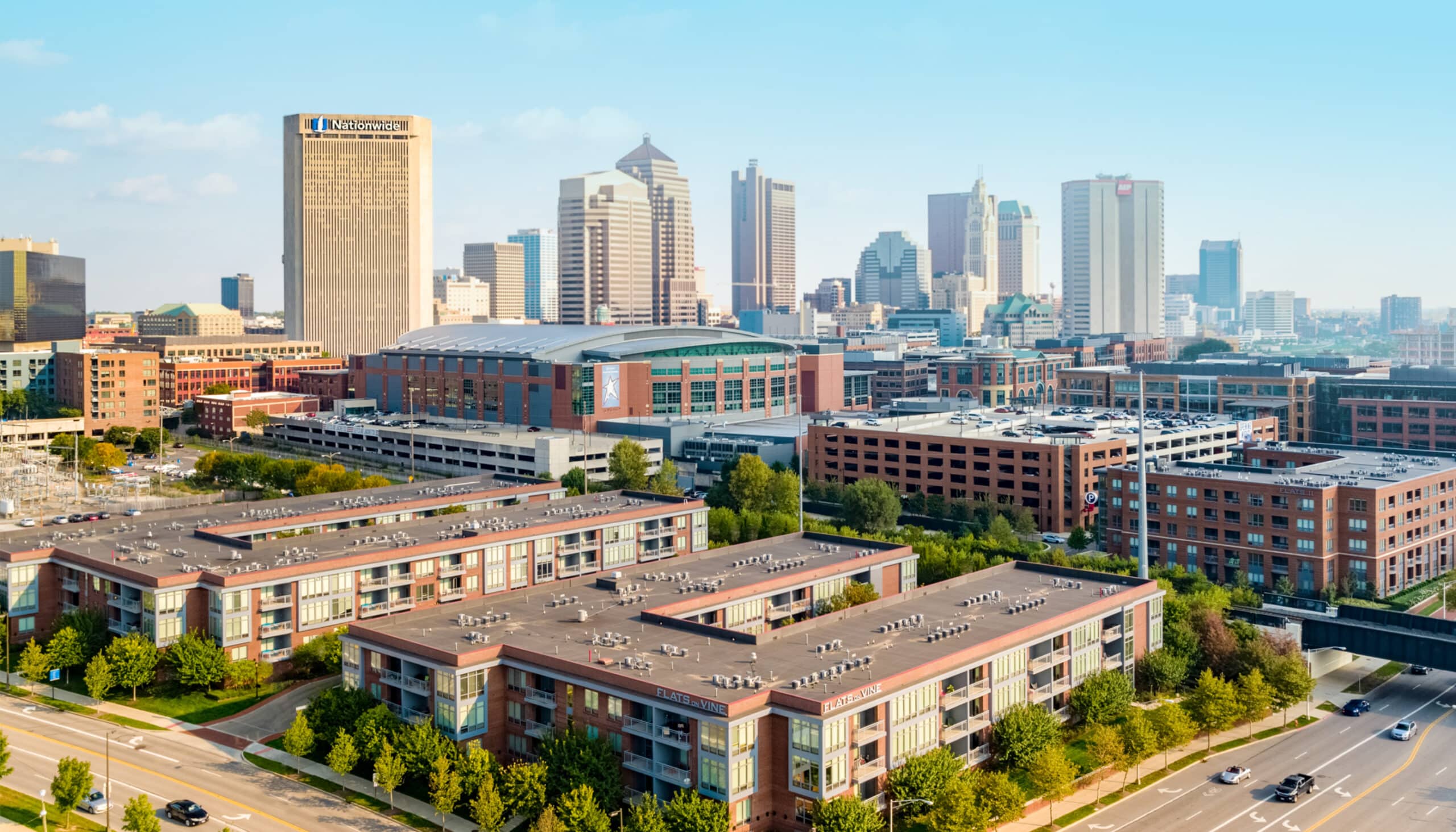 Aerial view of downtown Columbus, Ohio, featuring modern buildings, mid-rise apartments, and the city's skyline under a clear sky.