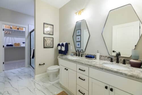 Modern bathroom with double sink vanity, granite countertop, octagonal mirrors, and black fixtures; open door reveals adjacent walk-in closet with shelves and hanging space.