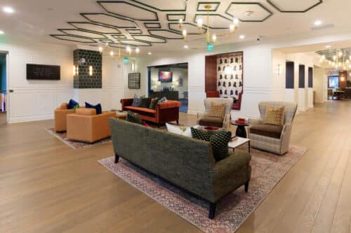 A modern lounge area with multiple sofas, armchairs, coffee tables, patterned rugs, and contemporary ceiling decor, featuring wall art and soft lighting.