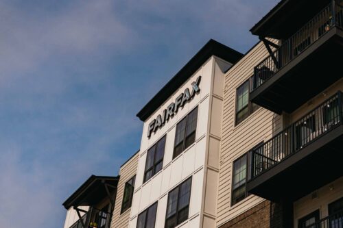 A multi-story apartment building with "FAIRFAX" on its facade, featuring balconies and modern architectural elements under a partly cloudy sky.